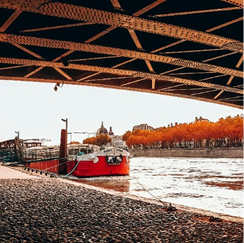 Bateau rouge amarré sous un pont, bord de rivière.